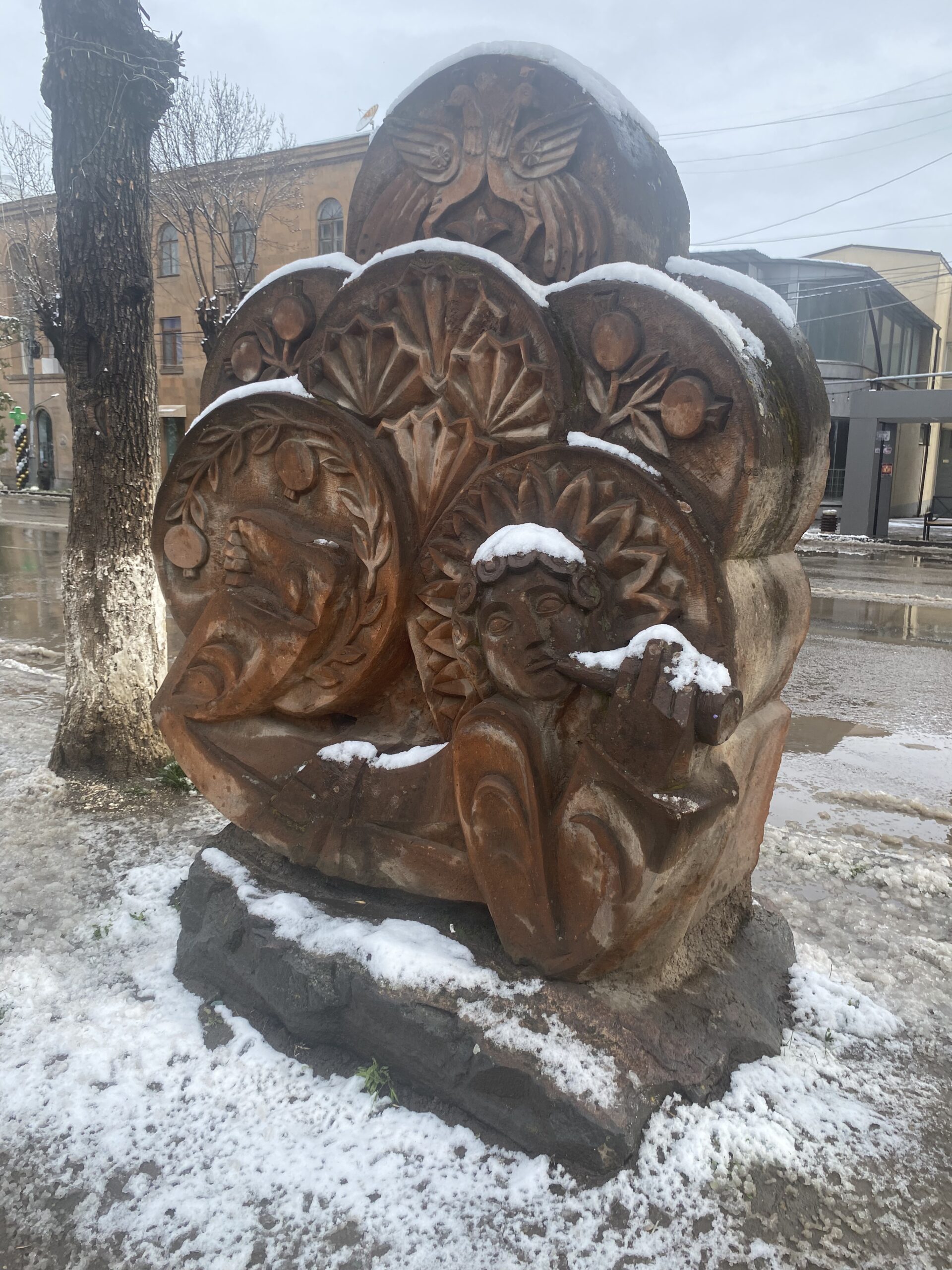 Escultura de fusta tallada amb relleus decoratius en un carrer de Vanadzor, coberta de neu