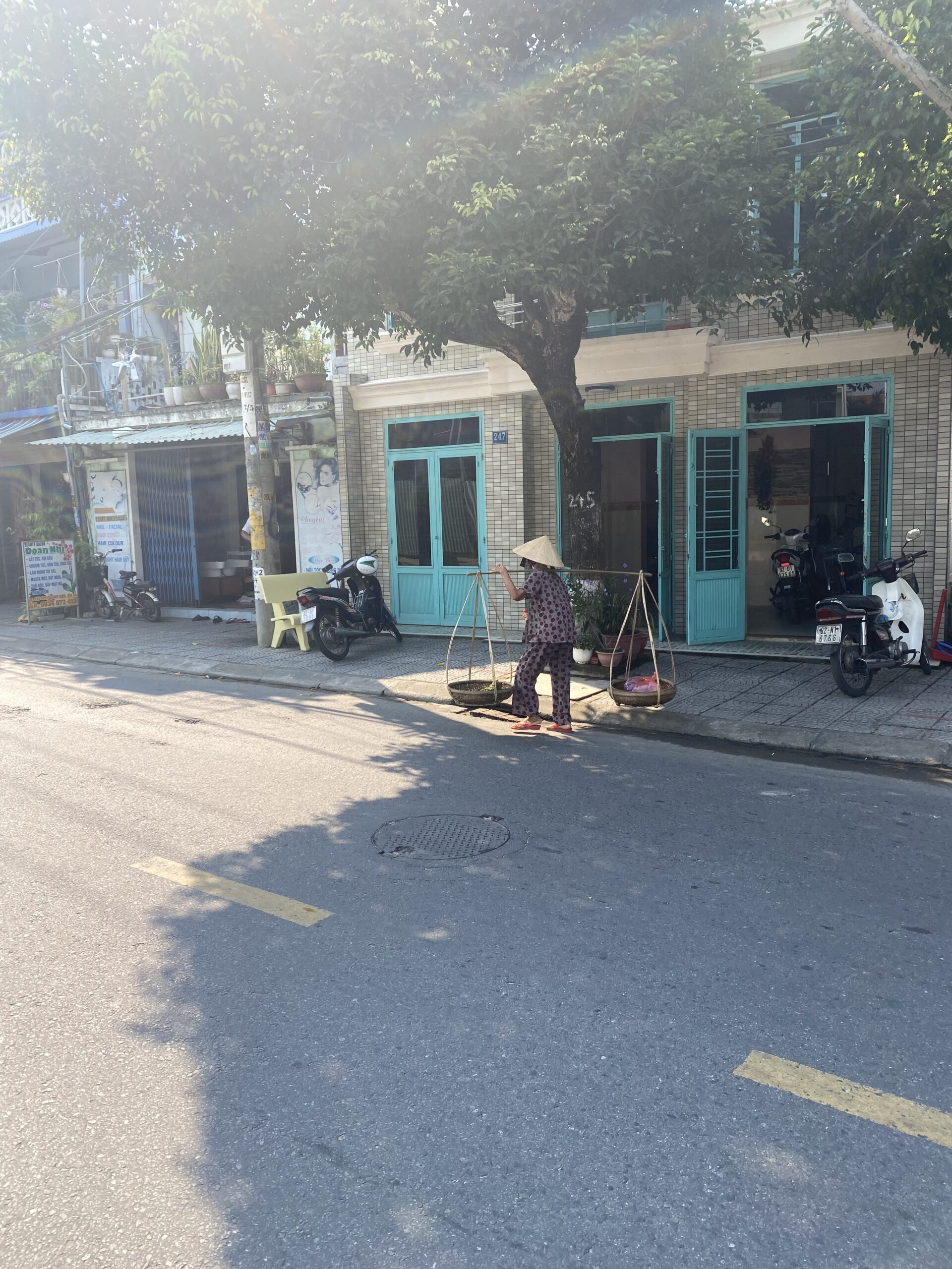 Carrer quotidià a Hoi An Carrer amb motos aparcades i una dona amb barret cònic vietnamita a Hoi An