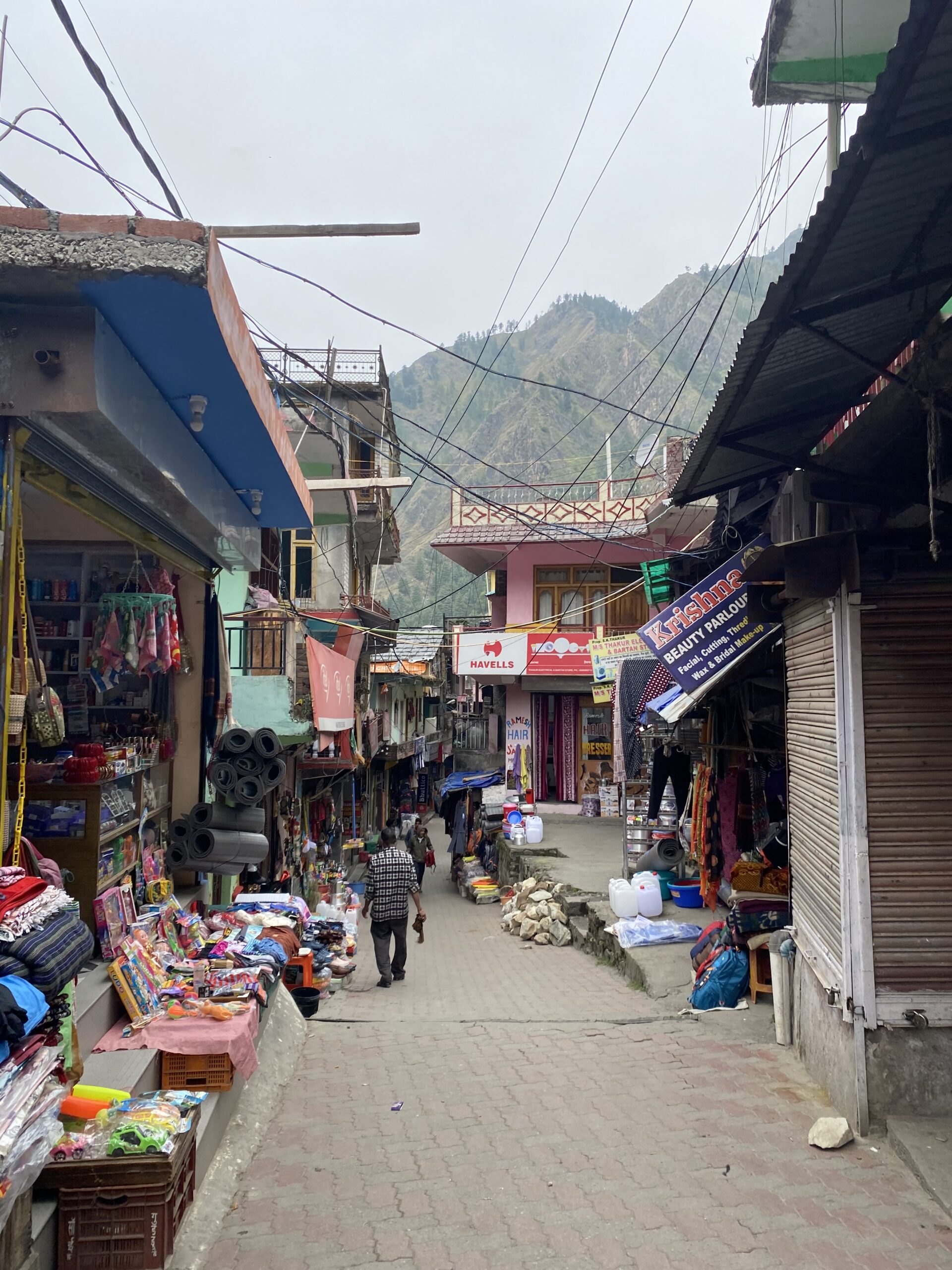 Carrer de Kasol amb petits comerços, allotjaments i muntanyes de la vall de Parvati al fons.