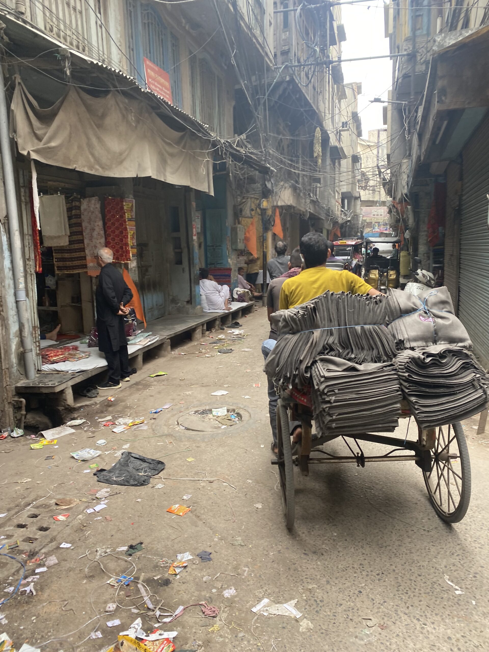 Carrer estret d'un mercat tradicional d'Amritsar amb comerciants, mercaderies i carros de transport.
