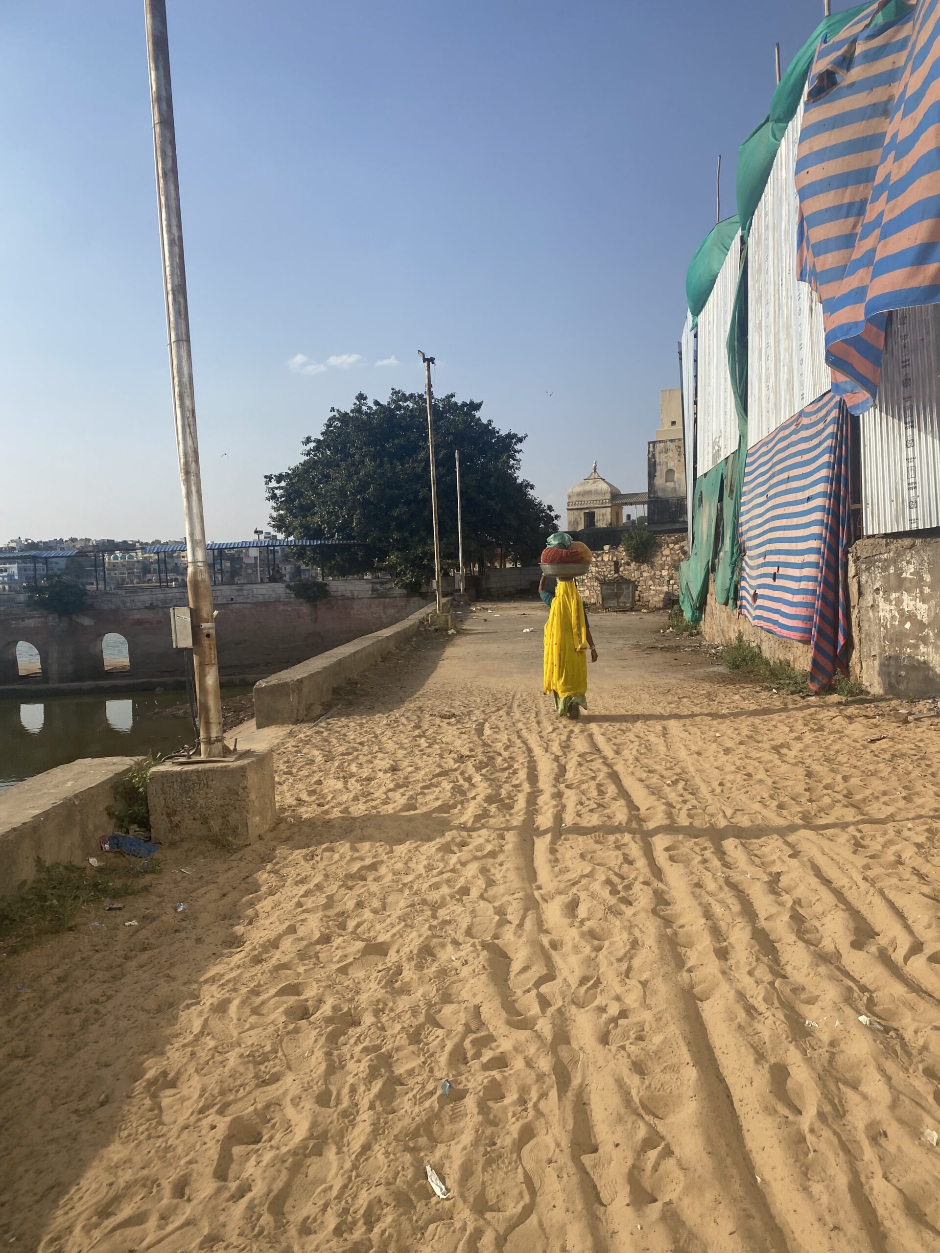 Dona caminant per un carrer tranquil de Pushkar envoltat d’edificis i murs tradicionals.