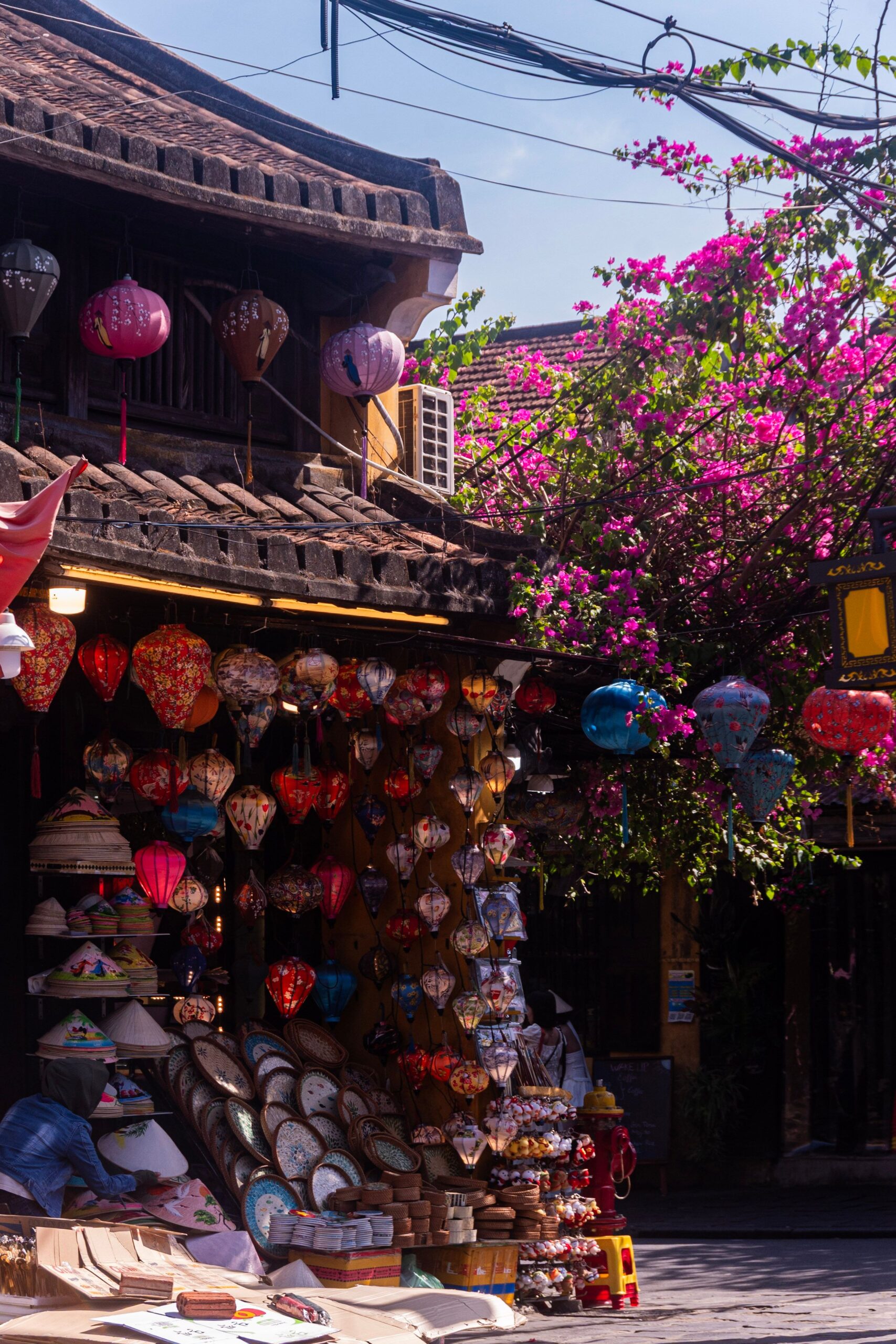 Llanternes i buguenvíl·lea a Hoi An Llanternes de colors penjades entre flors de buguenvíl·lea en un carrer de Hoi An, Vietnam