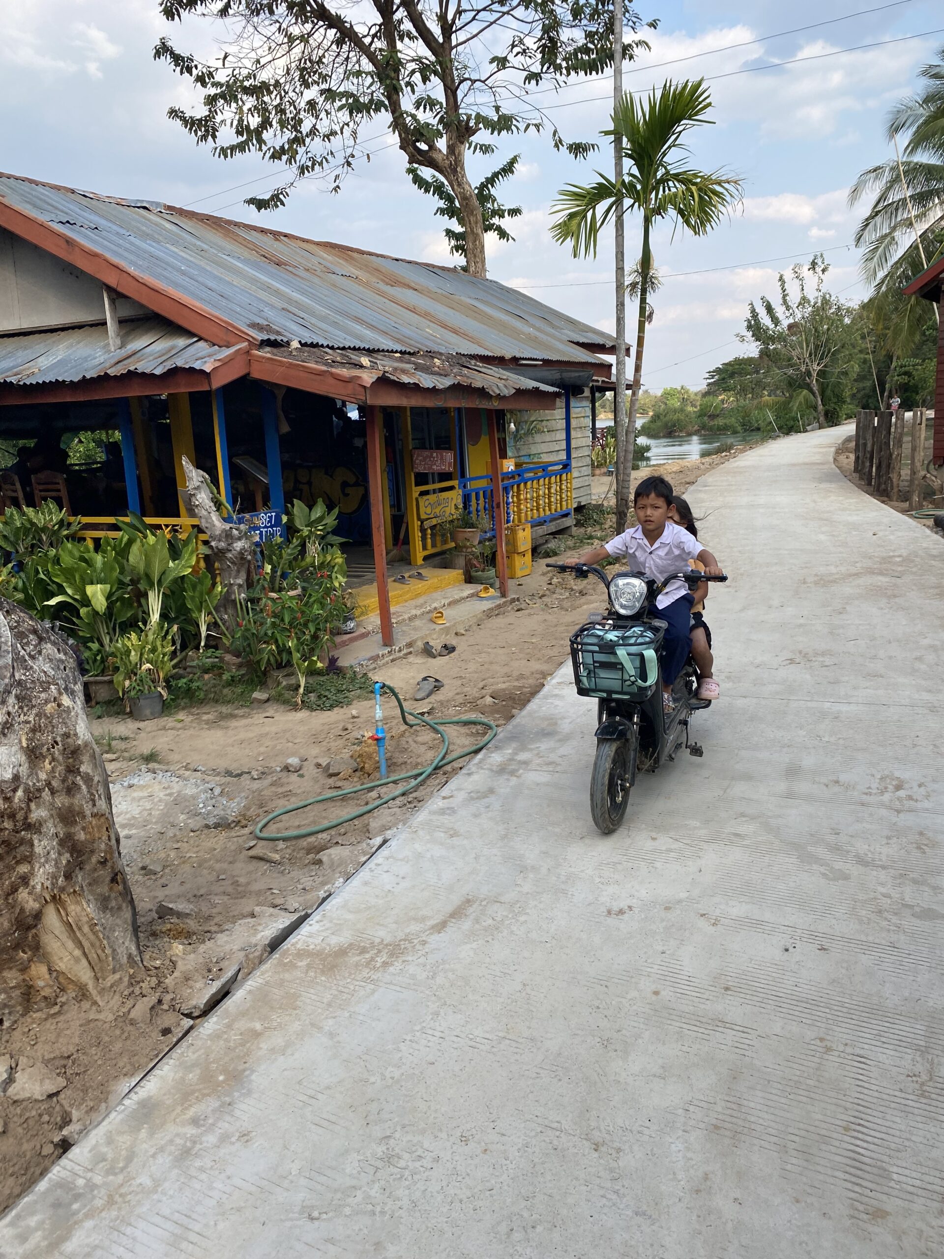 Camí amb botigues de fusta i una dona en moto a les illes del Mekong