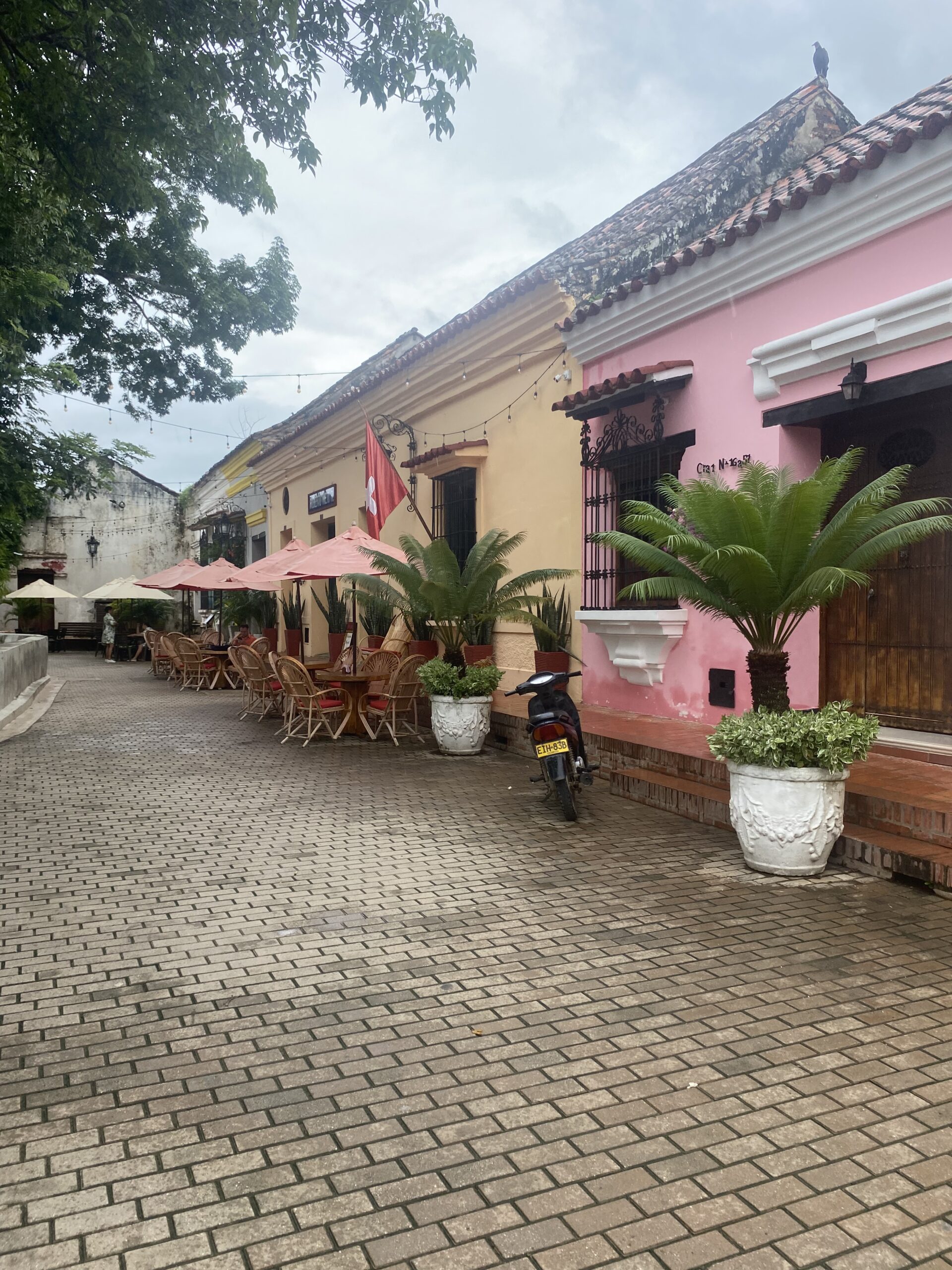 Carrer empedrat de Mompox amb una façana rosa, plantes i taules a l'exterior