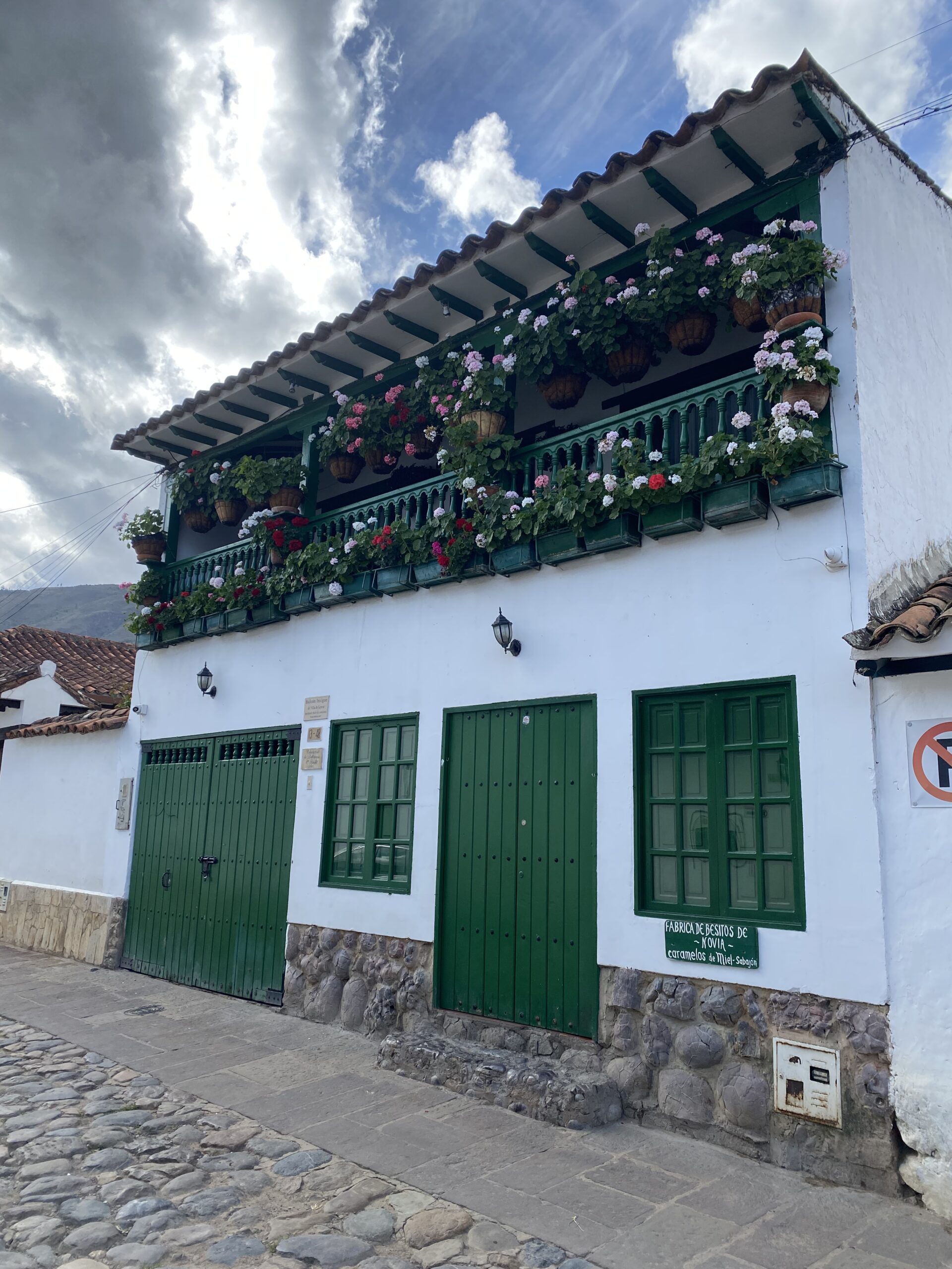 Casa colonial blanca amb portes verdes i balcons plens de plantes a Villa de Leyva