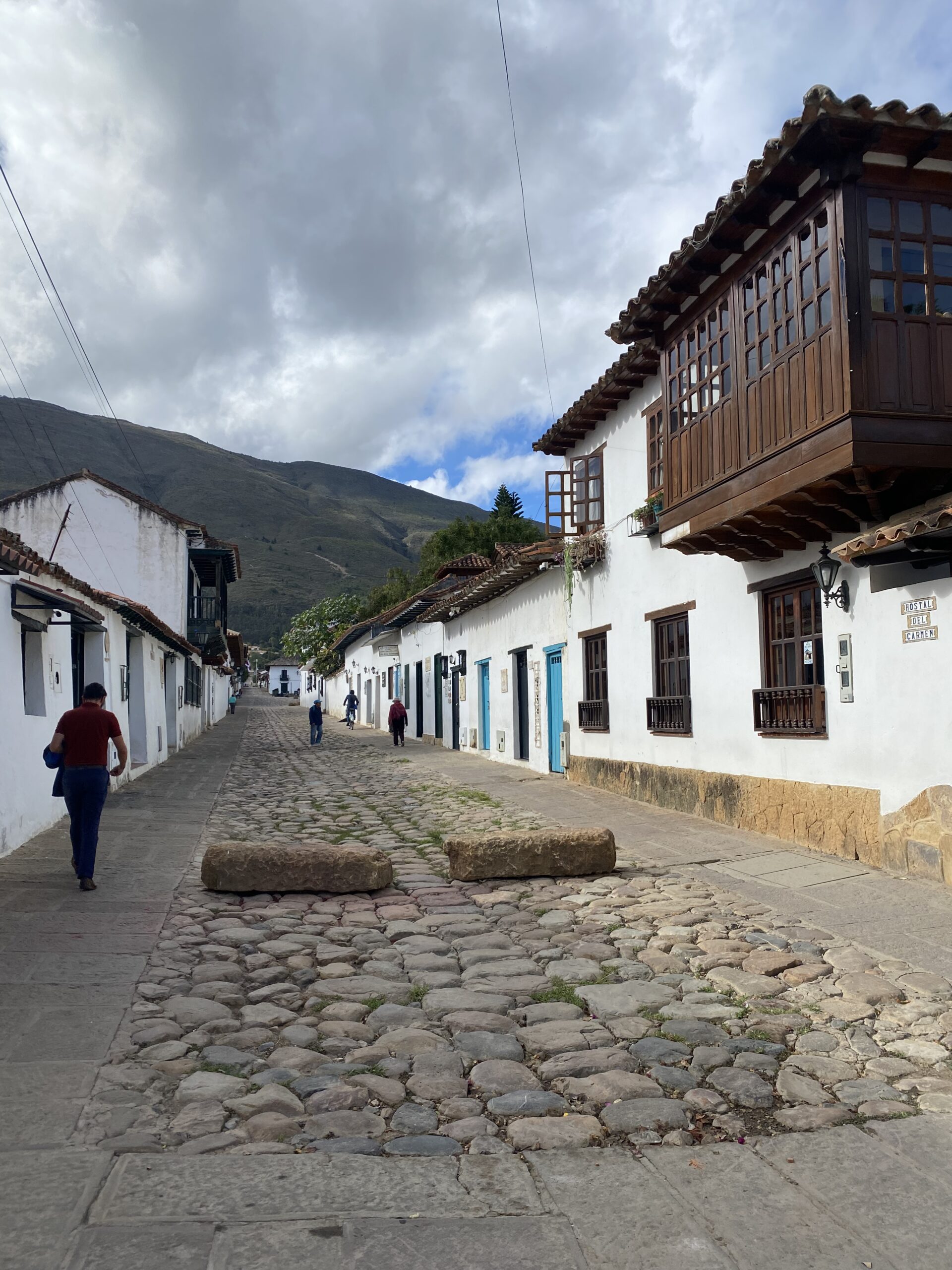 Persona caminant per un carrer empedrat de Villa de Leyva entre cases blanques amb balcons