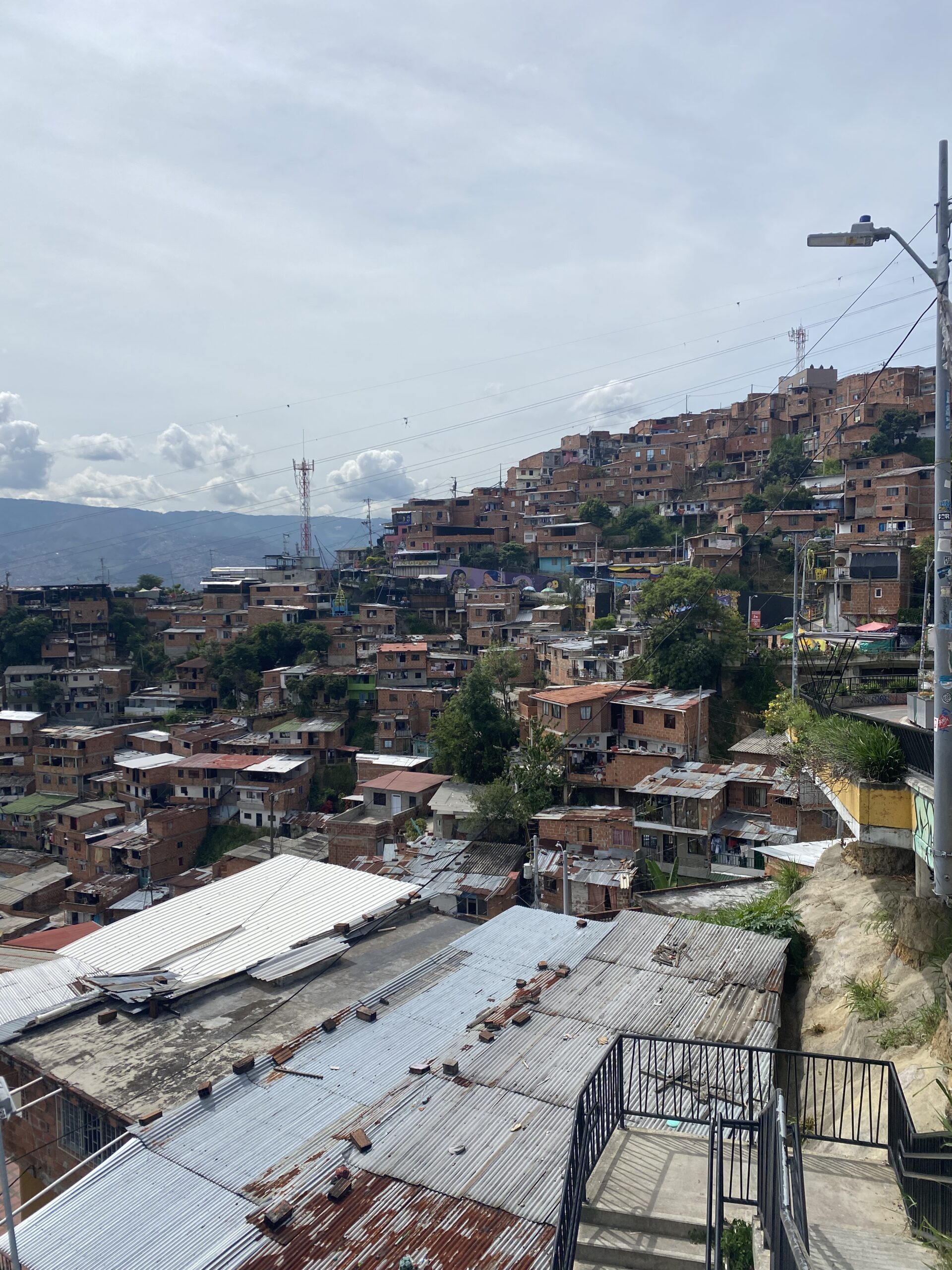 Vista de cases de maó i colors enfilades pel vessant d'un turó de Medellín, amb muntanyes al fons