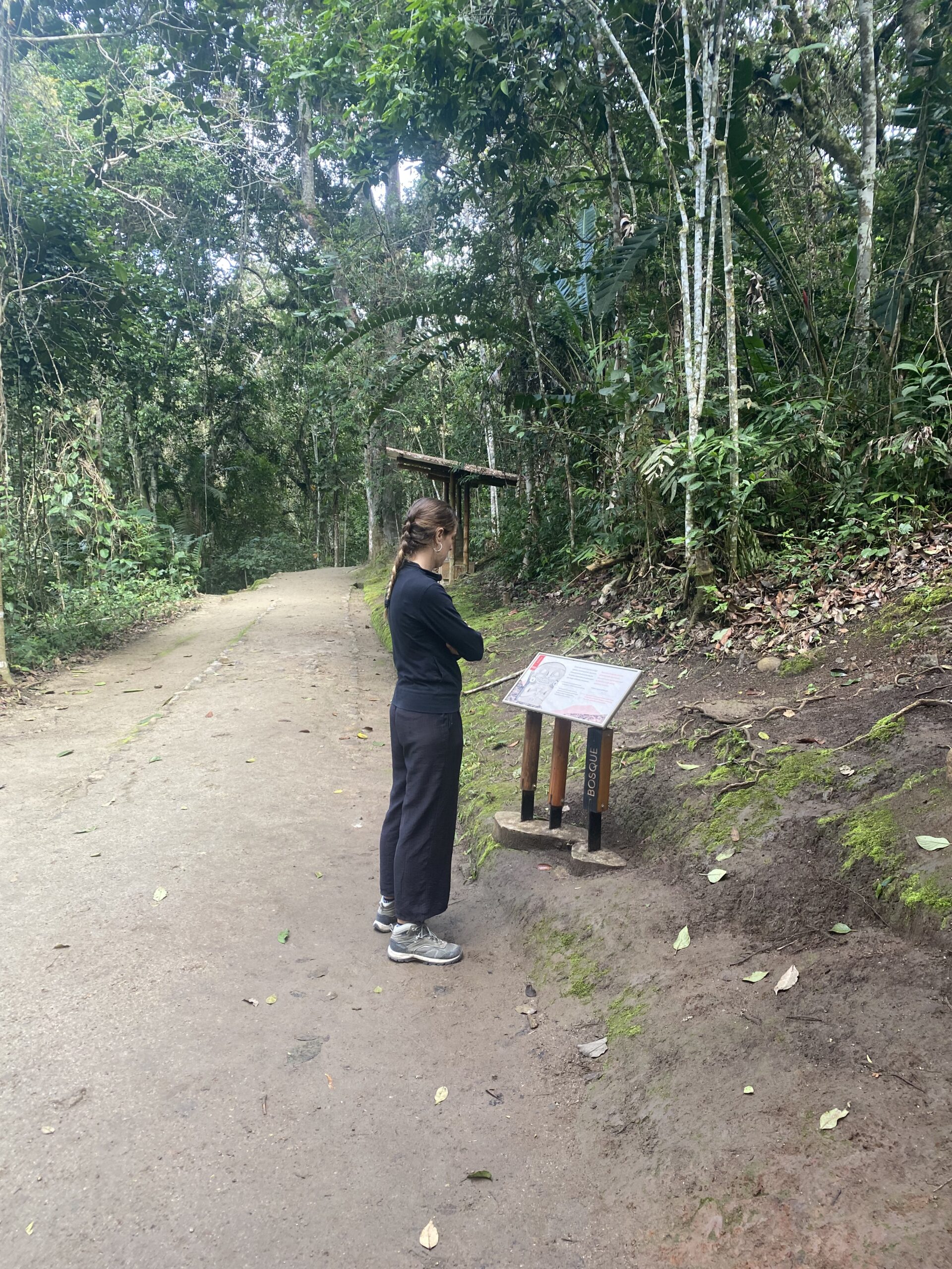 Un de nosaltres caminant per un sender de terra entre arbres alts, al costat d'un rètol informatiu del Parc Arqueològic de San Agustín