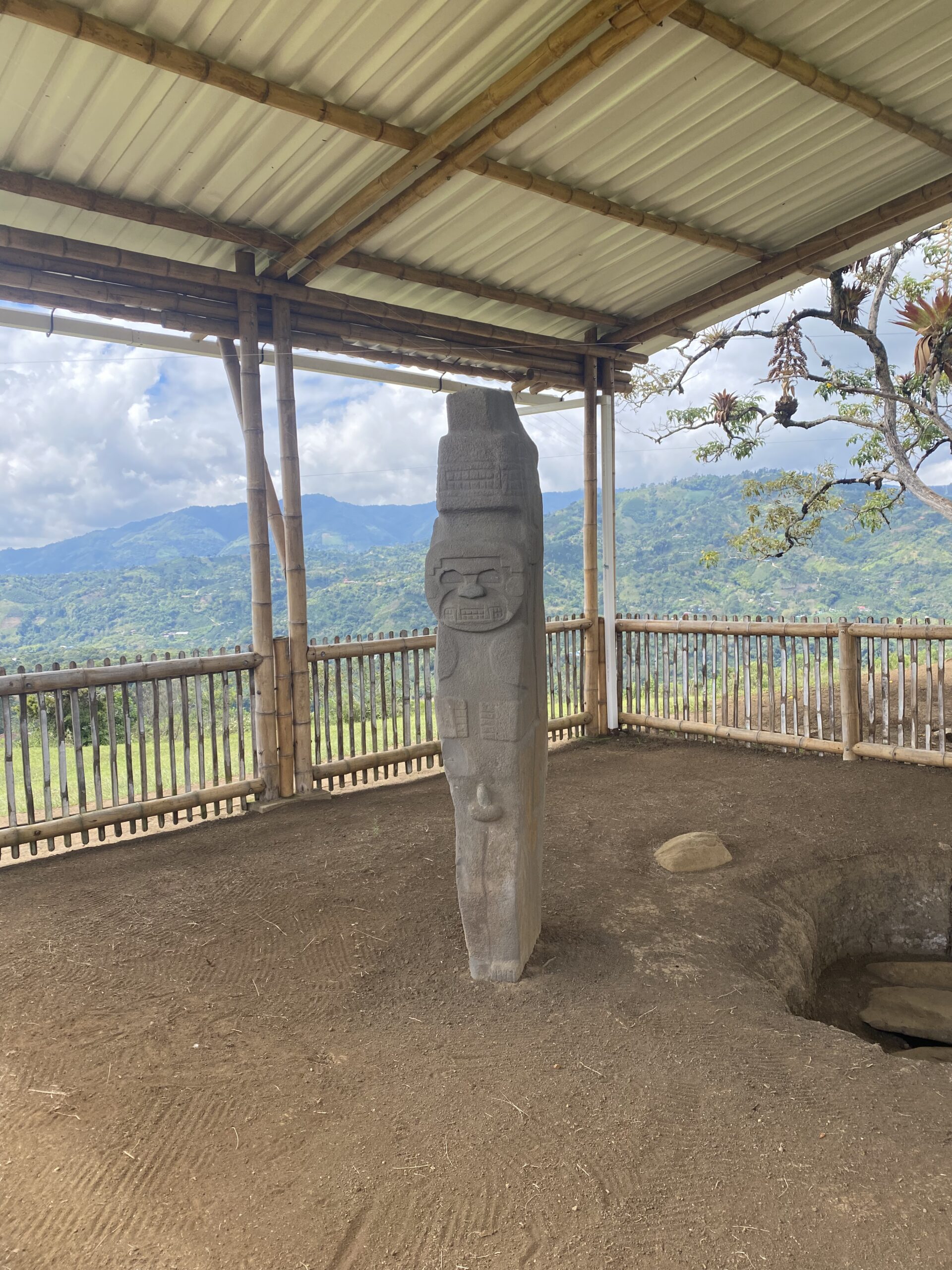 Estàtua de pedra sota un cobert de fusta, amb les muntanyes verdes del Macís Colombià al fons