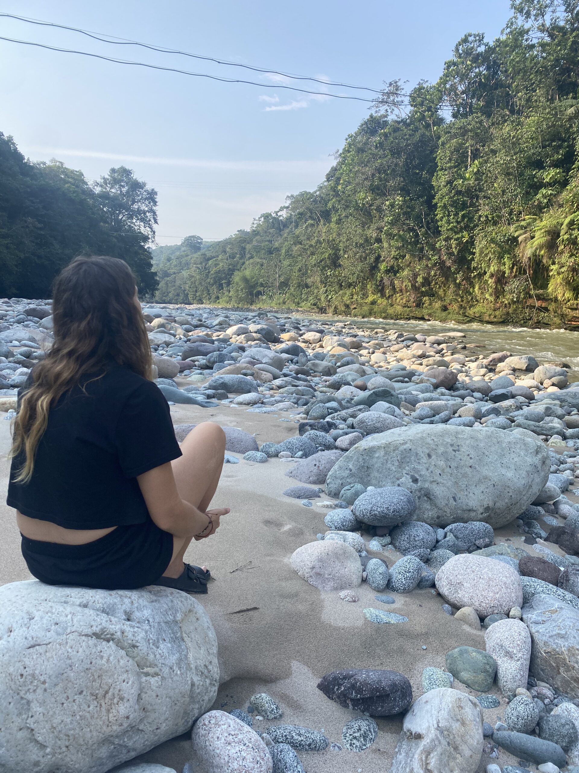 Una de nosaltres asseguda a la riba d'un riu de roques envoltat de selva, a Mocoa