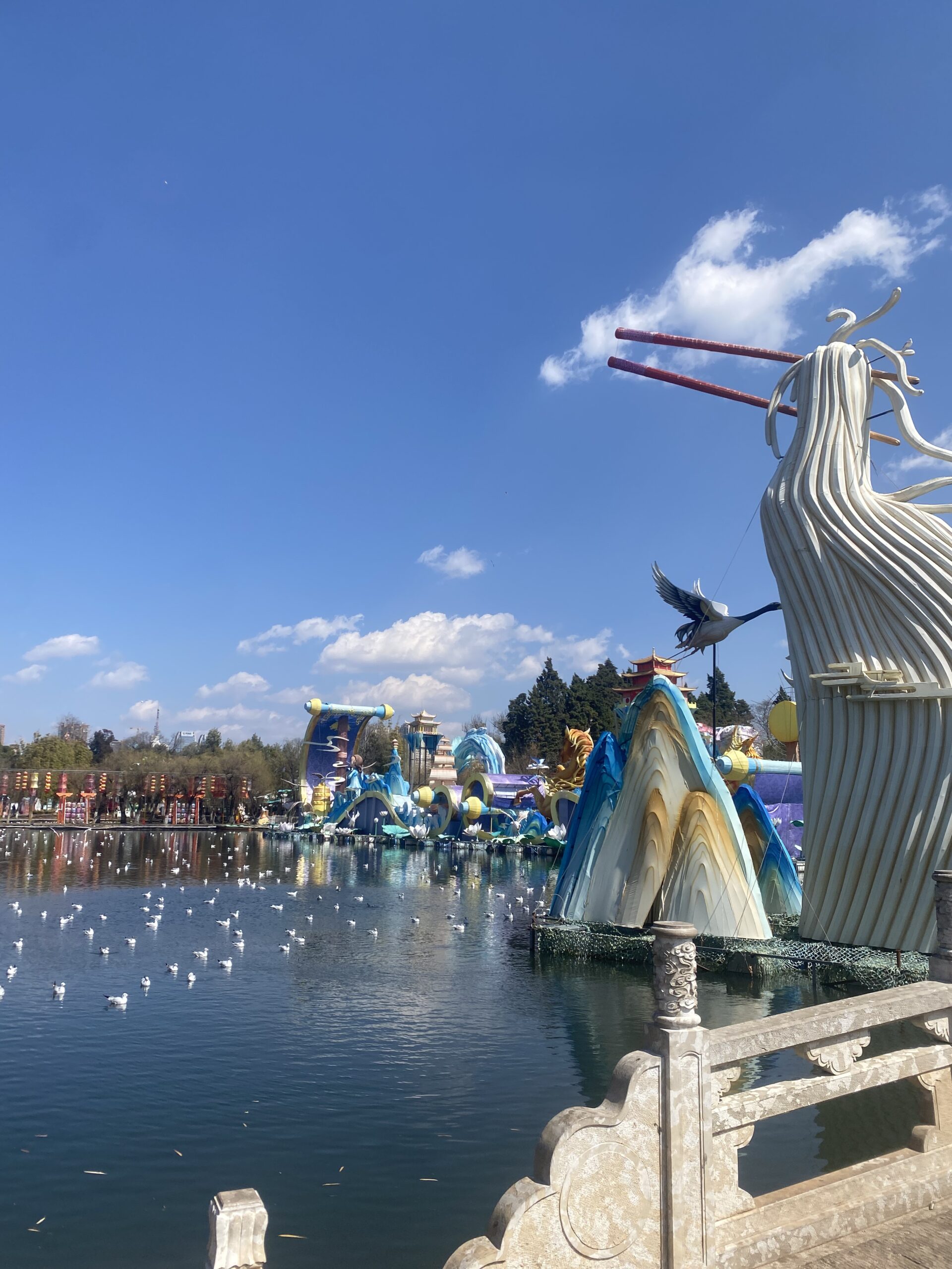 Escultura d'una au blanca i un ocell volant sota el cel blau de Kunming