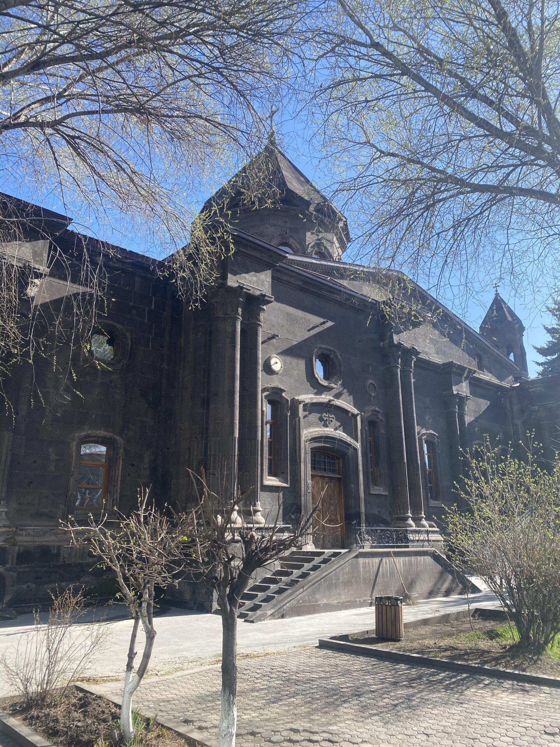 Església de pedra volcànica negra entre els arbres a Gyumri