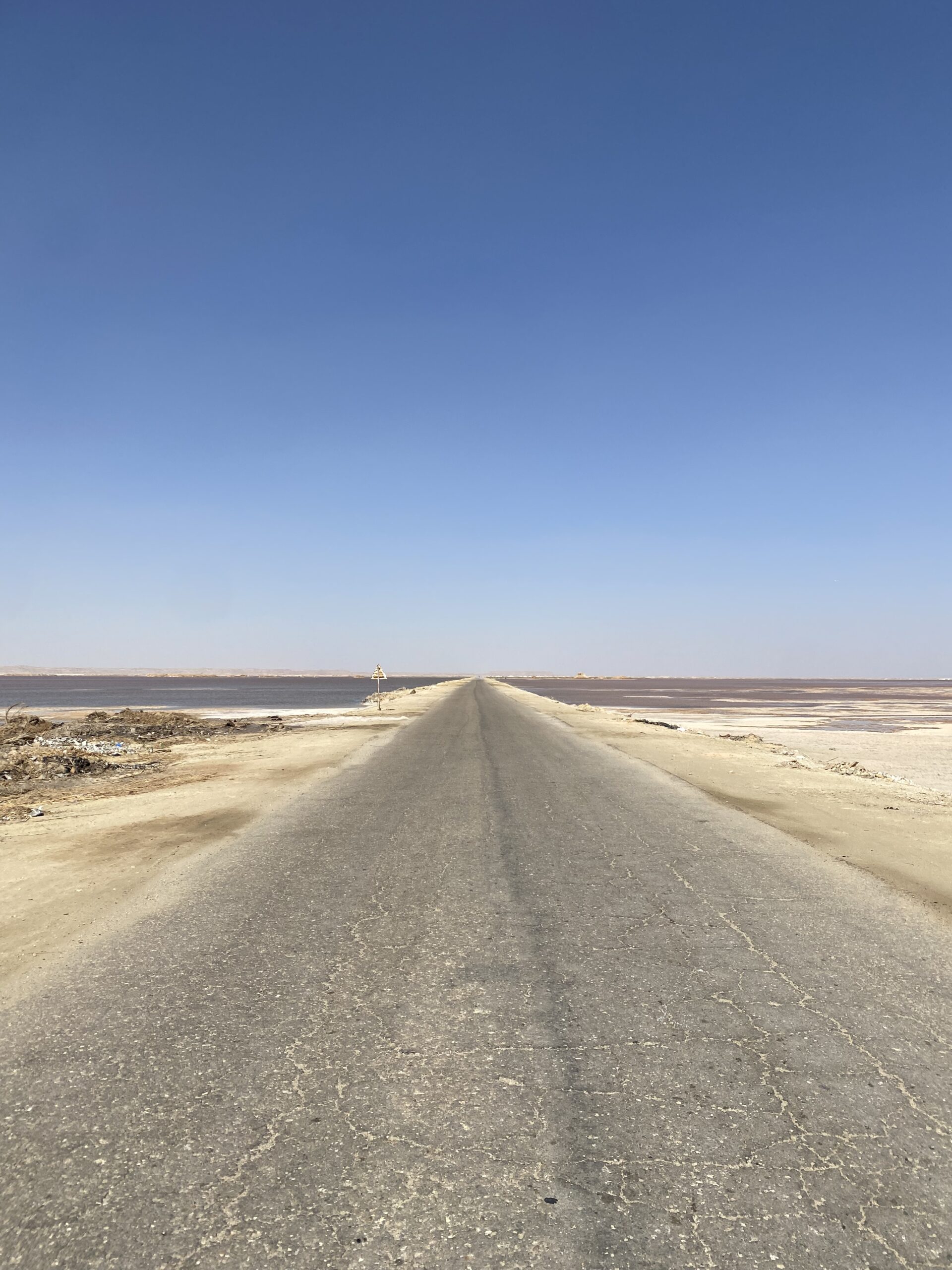 Carretera recta que travessa les planes de sal sota el cel blau a Siwa