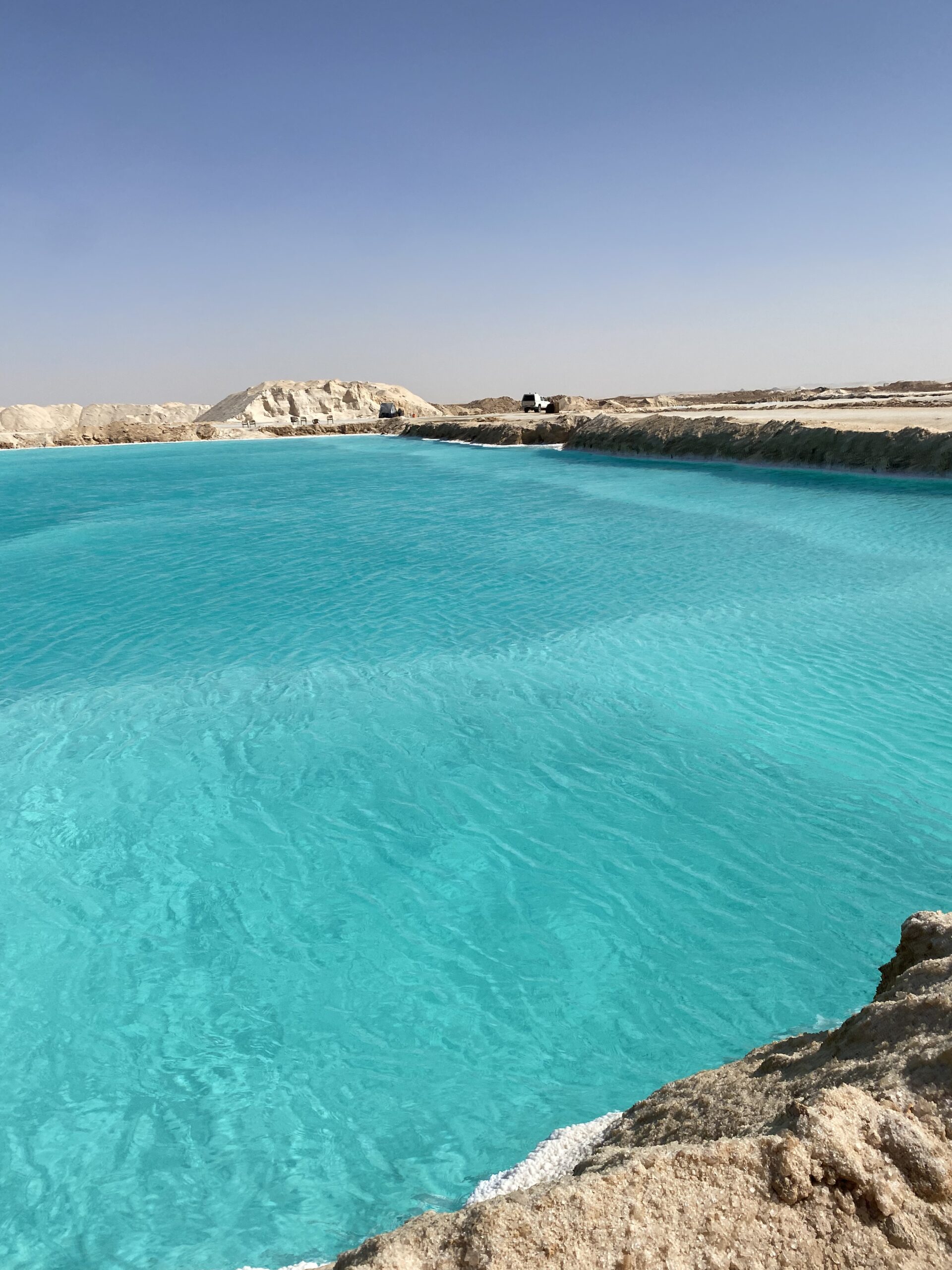 Aigües de color turquesa d'un llac salat de Siwa amb la riba blanca de sal